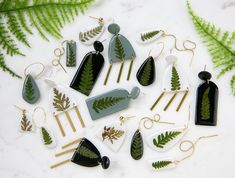 a collection of green and white earrings with leaf designs on them next to fern leaves