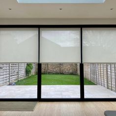 an open room with sliding glass doors and white roller shades on the windows looking outside