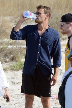 a man drinking water from a bottle while standing next to other people on the beach