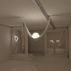 an empty room with two suspended lights and white curtains on the walls, in front of a circular window