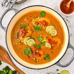 a large pot filled with soup and garnished with cilantro, limes, and other ingredients