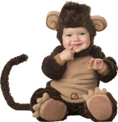 a baby wearing a monkey costume sitting on the ground with his hands in his mouth