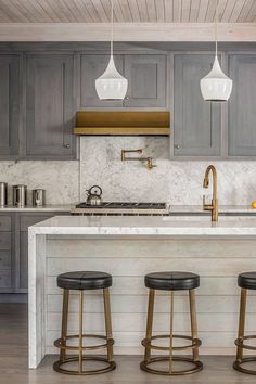 three stools sit in front of an island with marble countertops and gray cabinets