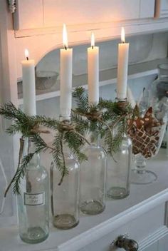 candles are lit in glass bottles with pine branches on the top and bottom, sitting on a dresser