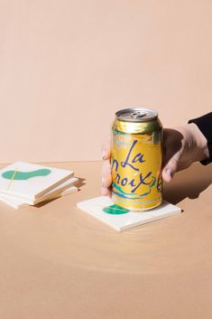 a hand holding a can of la croixe on top of a table next to coasters