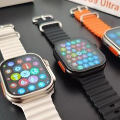 three smart watches sitting next to each other on top of a black table with orange and white straps