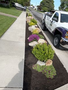 a white truck parked on the side of a road next to a flower bed filled with flowers