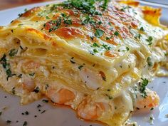 a white plate topped with lasagna covered in cheese and shrimp meats, garnished with parsley