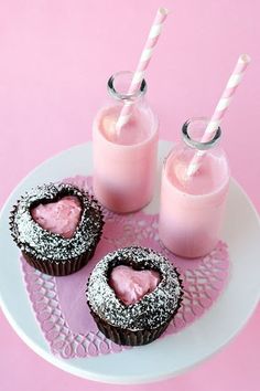 three cupcakes on a plate with two cups of milk