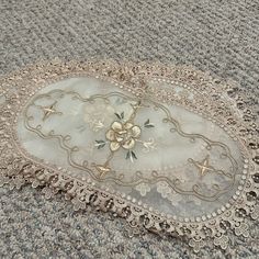 an old lace doily with flowers on it laying on the floor in front of a carpet