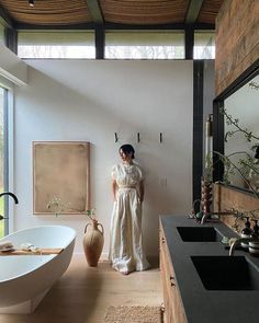 a woman standing in a bathroom next to a bathtub and large mirror on the wall