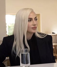 a woman sitting at a table with a glass in front of her and looking off to the side