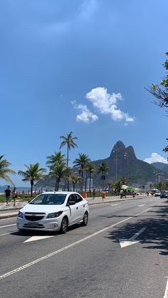 a white car driving down a street next to tall palm trees and a mountain in the background