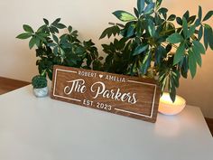 a wooden sign sitting on top of a white table next to a potted plant