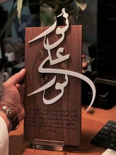 a person holding up a wooden plaque with arabic writing on it, in front of a computer keyboard