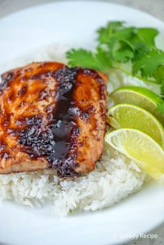 a white plate topped with rice and meat covered in bbq sauce next to lime wedges