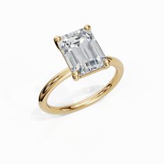 a yellow gold ring with an emerald cut diamond in the center, on a white background