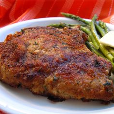 a white plate topped with meat and asparagus on top of a red table cloth