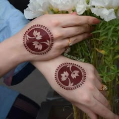 two women with henna tattoos on their hands next to some flowers and greenery