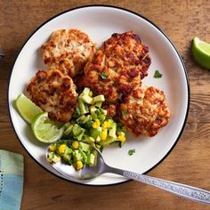 three crab cakes on a white plate next to a side of salad and lime wedges