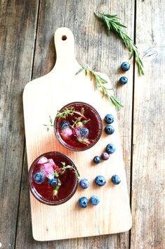 two glasses filled with blueberries on top of a cutting board next to rosemary sprigs