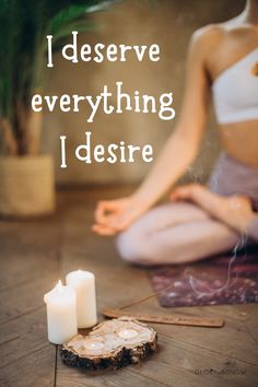 a woman sitting on the floor in front of a candle with her hands up to her chest