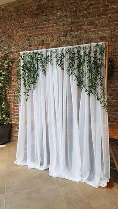 a white curtain with green plants on it in front of a brick wall and wooden bench