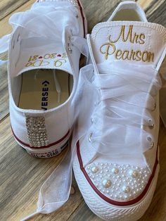 two pairs of white shoes with bows and pearls on the bottom, one is decorated with gold lettering