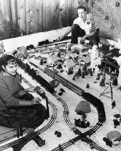 two boys are playing with toy trains in the snow while another boy looks at them