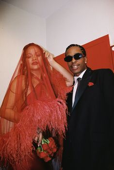 a man in a suit and sunglasses standing next to a woman wearing a red veil