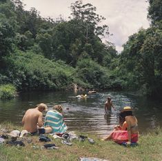 several people are sitting in the water near some trees and towels on the ground,