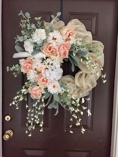 a wreath is hanging on the front door with flowers and greenery around it,