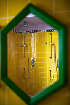 the reflection of a shower head in a green and yellow tiled bathroom mirror, which is reflecting it's surroundings