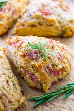 several biscuits with cheese and herbs on them sitting on a cutting board next to rosemary sprigs