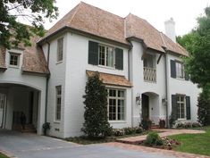 a large white house with green shutters on the front and side windows, surrounded by greenery