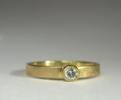 a yellow gold ring with a single diamond in the center, sitting on a white surface