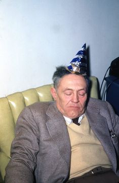 an older man wearing a party hat while sitting in a chair with his eyes closed