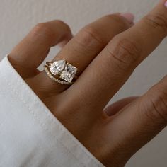 a woman's hand with a gold ring and two diamond engagement rings on it