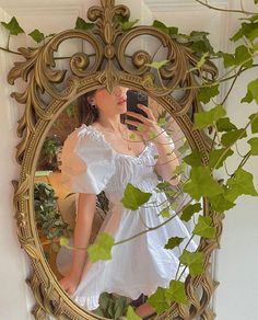 a woman taking a selfie in front of a mirror with ivy growing on it