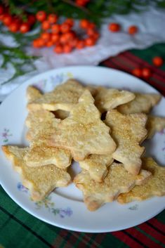 some cookies are on a white plate with red berries in the background and green table cloth