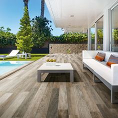 an outdoor living room with wood flooring and white furniture next to a swimming pool