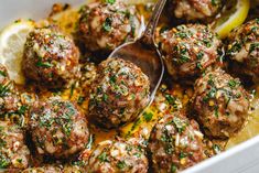 a close up of meatballs in a pan with lemon wedges