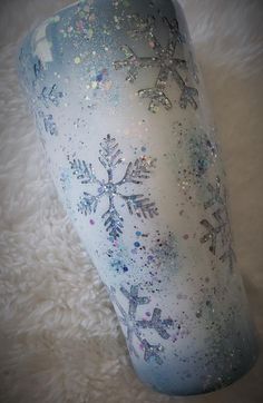 a blue vase with snowflakes on it sitting on a white fur covered floor