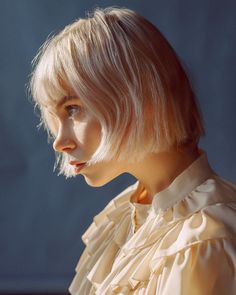 a woman with blonde hair wearing a white blouse and gold earring, looking off to the side