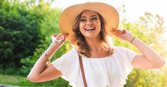 a woman wearing a straw hat and holding her hands behind her head, smiling at the camera