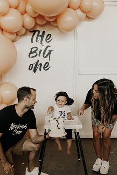 a baby sitting in a high chair next to two adults