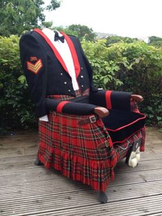 a man in a kilt sitting on top of a wooden bench next to bushes