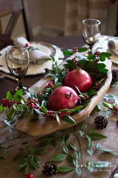 two pomegranates in a wooden bowl with greenery and pine cones