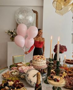 a woman standing in front of a table filled with cake and balloons