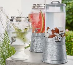 three metal buckets filled with watermelon and other drinks sitting on top of a table